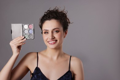 Photo of Smiling woman with eyeshadow palette on grey background. Space for text