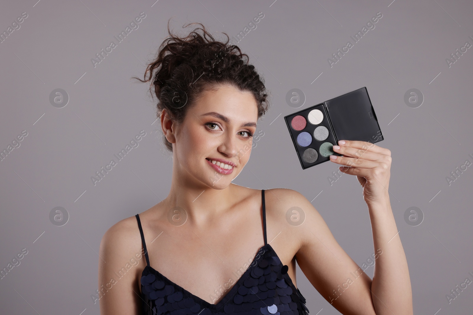 Smiling woman with eyeshadow palette on grey background Photo of Smiling woman with eyeshadow palette on grey background