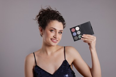 Photo of Smiling woman with eyeshadow palette on grey background