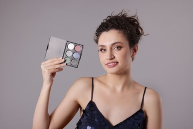 Photo of Smiling woman with eyeshadow palette on grey background