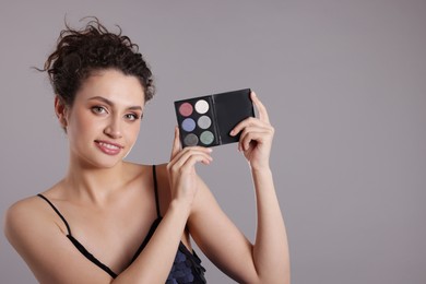 Photo of Smiling woman with eyeshadow palette on grey background. Space for text