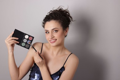 Photo of Smiling woman with eyeshadow palette and brush on grey background. Space for text