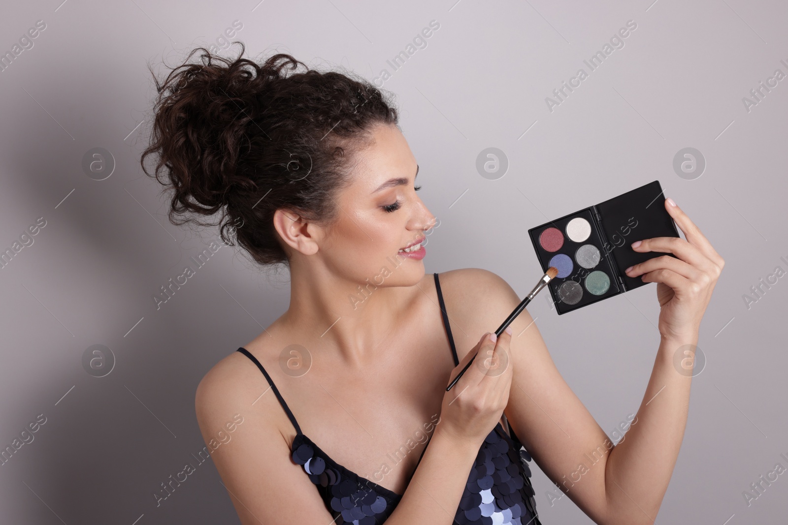 Smiling woman with eyeshadow palette and brush on grey background Photo of Smiling woman with eyeshadow palette and brush on grey background