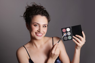 Photo of Smiling woman with eyeshadow palette and brush on grey background