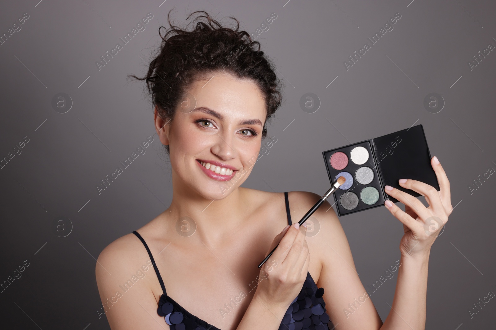 Smiling woman with eyeshadow palette and brush on grey background Photo of Smiling woman with eyeshadow palette and brush on grey background