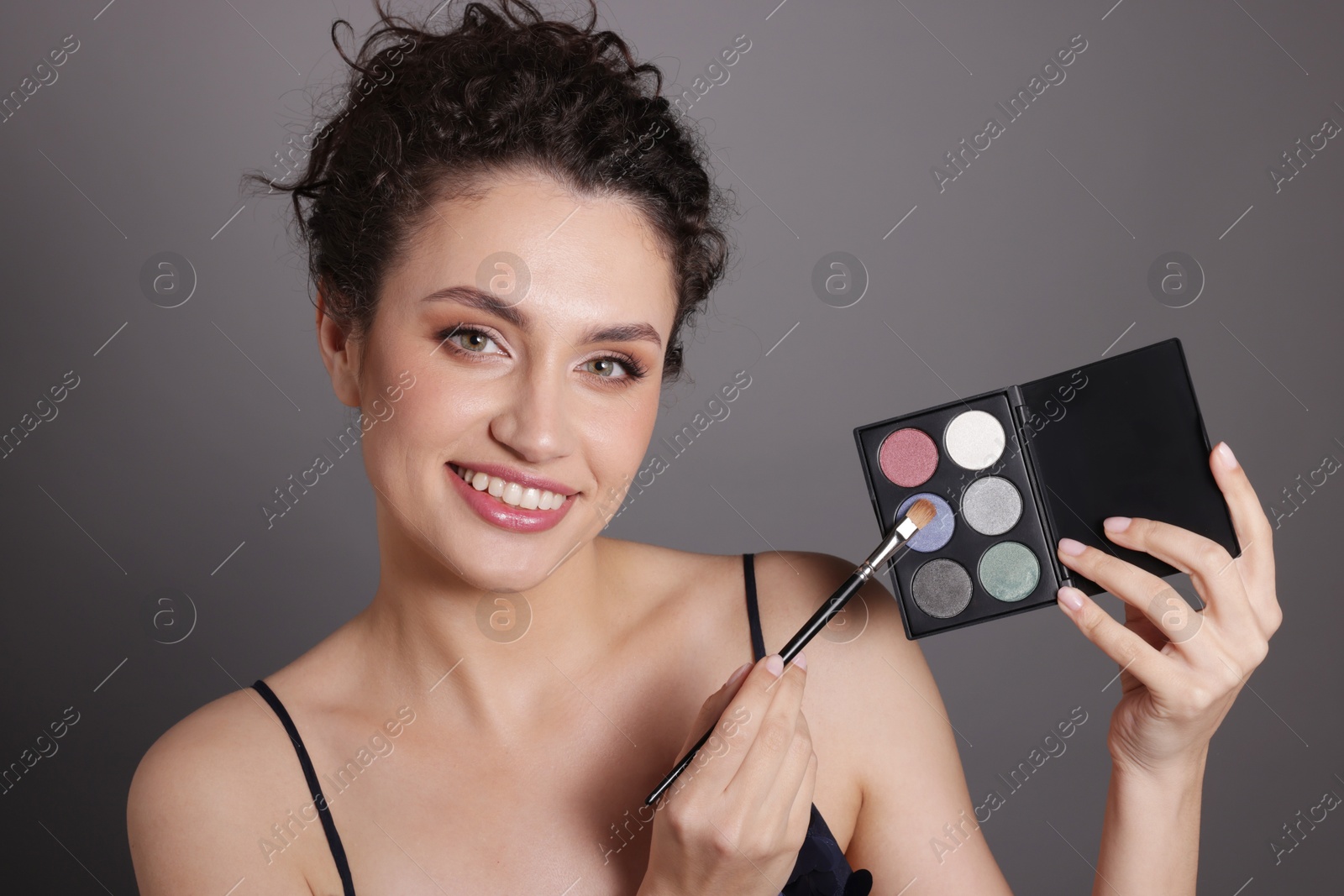 Smiling woman with eyeshadow palette and brush on grey background Photo of Smiling woman with eyeshadow palette and brush on grey background