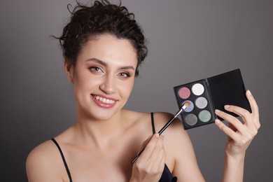 Photo of Smiling woman with eyeshadow palette and brush on grey background