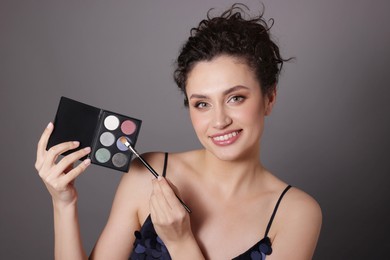 Photo of Smiling woman with eyeshadow palette and brush on grey background