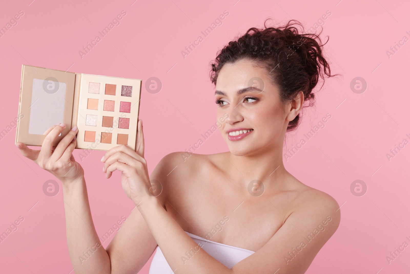 Smiling woman with eyeshadow palette on pink background Photo of Smiling woman with eyeshadow palette on pink background