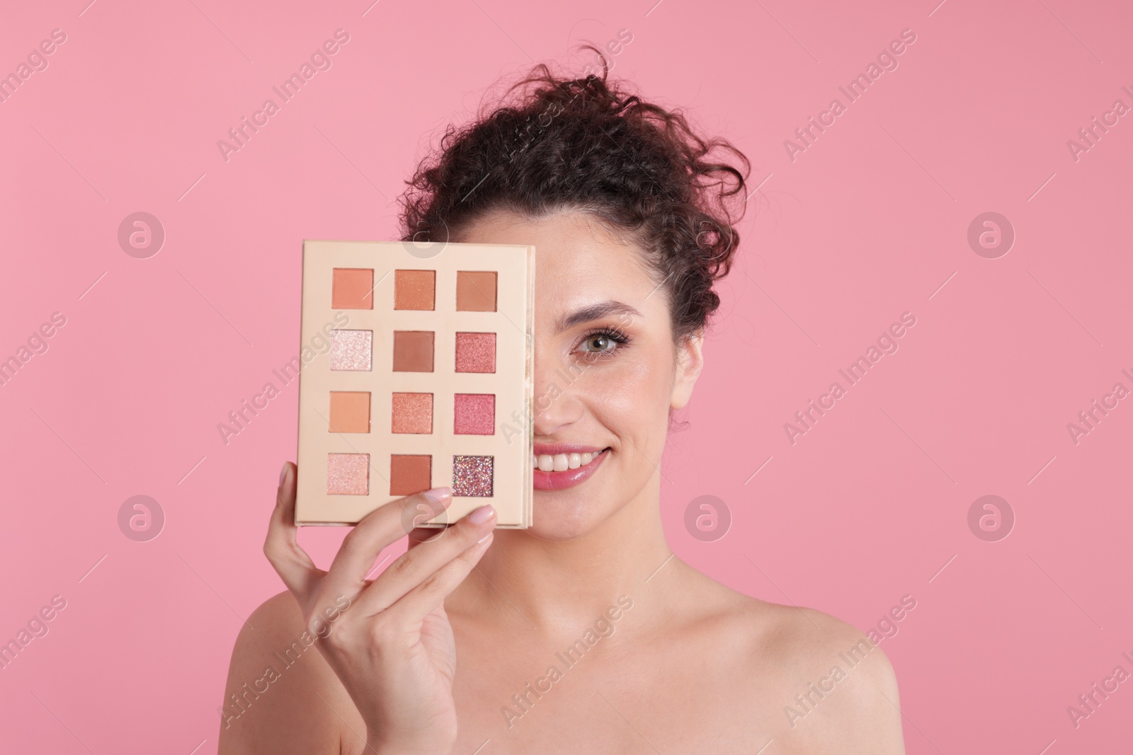 Smiling woman covering eye with eyeshadow palette on pink background Photo of Smiling woman covering eye with eyeshadow palette on pink background