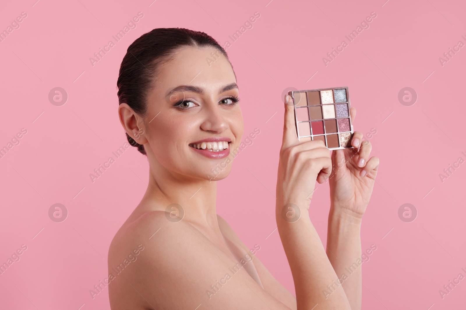 Smiling woman with eyeshadow palette on pink background Photo of Smiling woman with eyeshadow palette on pink background