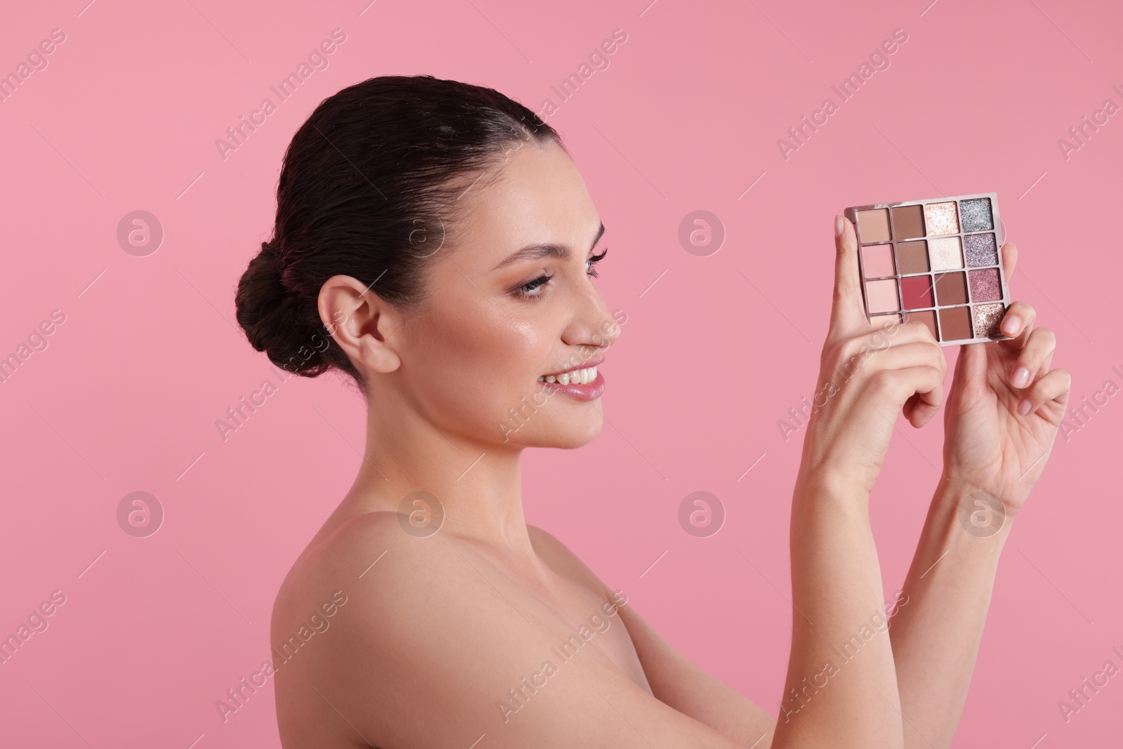 Smiling woman with eyeshadow palette on pink background Photo of Smiling woman with eyeshadow palette on pink background