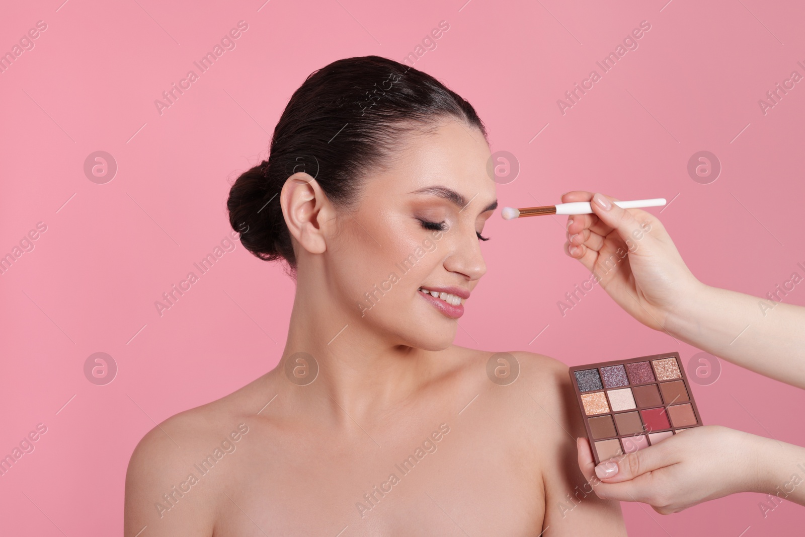 Makeup artist applying eyeshadows onto woman's face on pink background, closeup Photo of Makeup artist applying eyeshadows onto woman's face on pink background, closeup