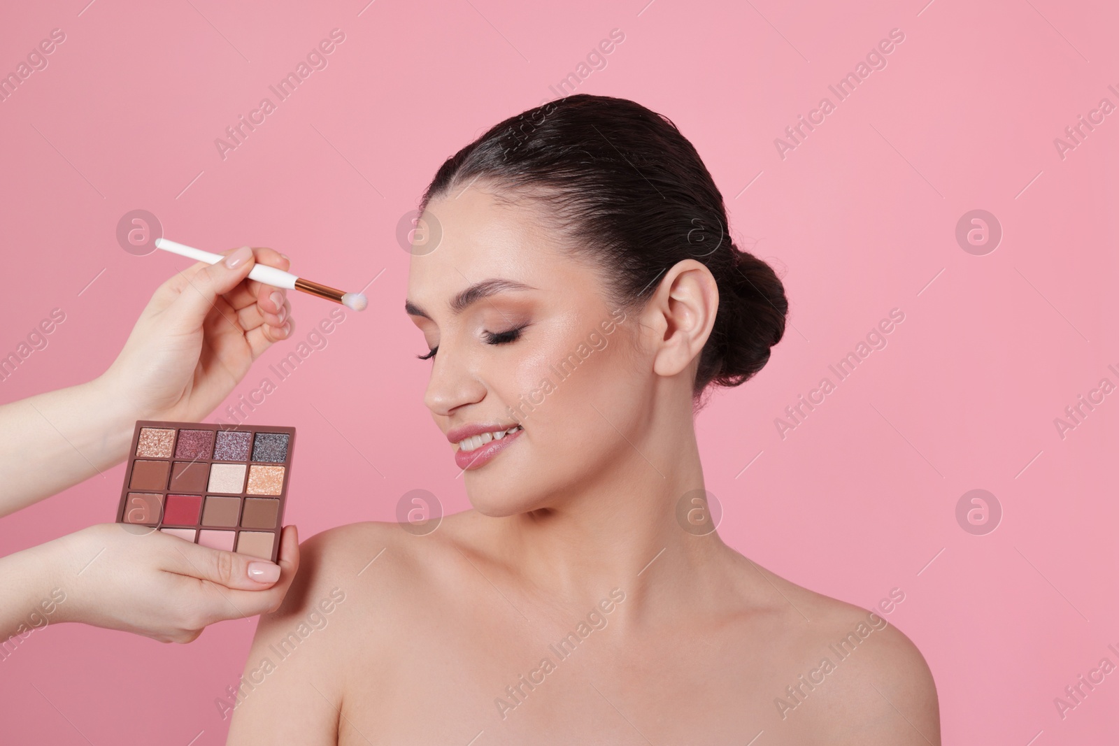 Makeup artist applying eyeshadows onto woman's face on pink background, closeup Photo of Makeup artist applying eyeshadows onto woman's face on pink background, closeup