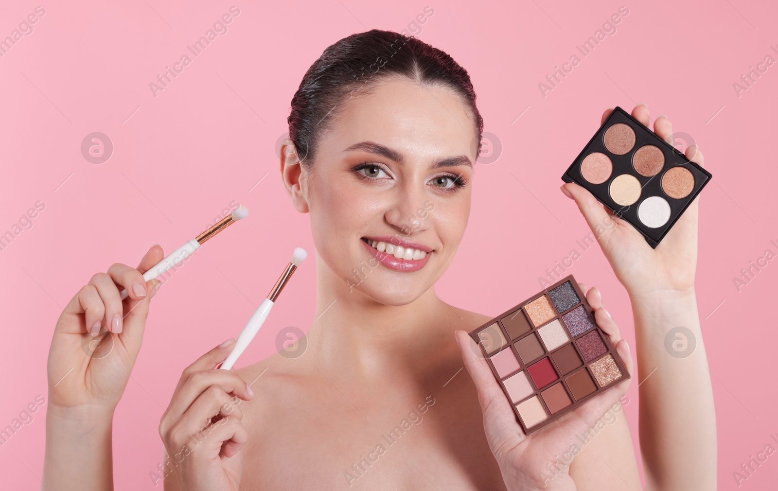 Makeup artist with eyeshadow palettes, brushes and smiling woman on pink background, closeup Photo of Makeup artist with eyeshadow palettes, brushes and smiling woman on pink background, closeup
