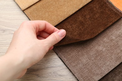 Photo of Woman with samples of different fabrics at wooden table, closeup