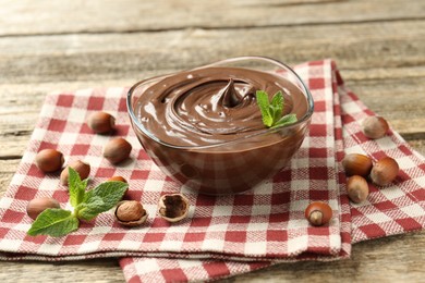 Photo of Tasty chocolate spread with mint and hazelnuts on wooden table, closeup