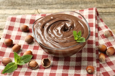 Photo of Tasty chocolate spread with mint and hazelnuts on wooden table, closeup
