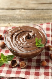 Photo of Tasty chocolate spread with mint and hazelnuts on wooden table, closeup