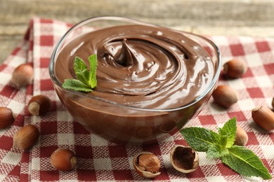 Photo of Tasty chocolate spread with mint and hazelnuts on table, closeup