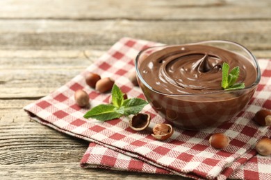 Photo of Tasty chocolate spread with mint and hazelnuts on wooden table, closeup. Space for text