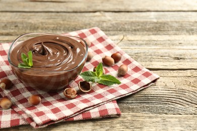 Photo of Tasty chocolate spread with mint and hazelnuts on wooden table, closeup. Space for text