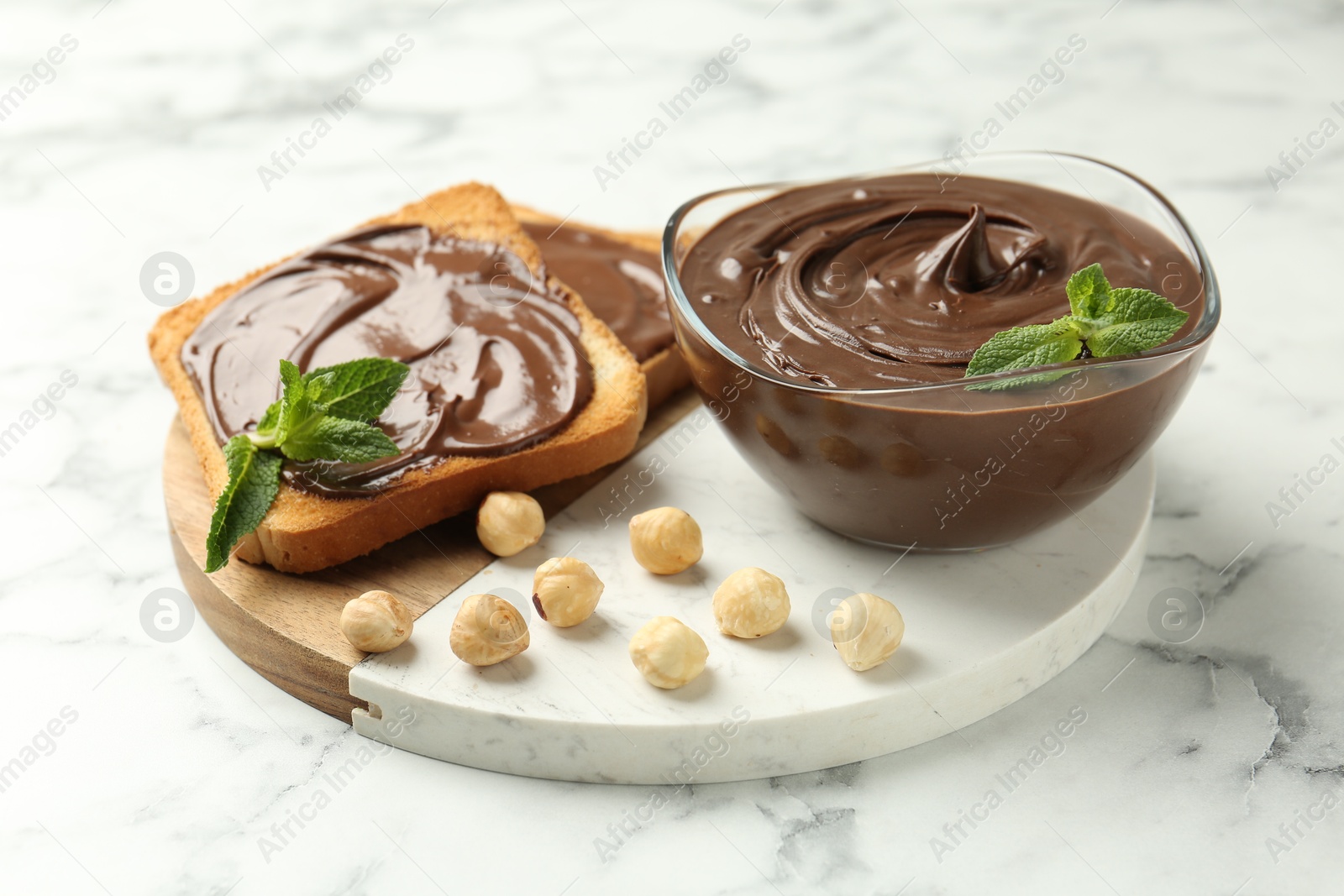 Tasty chocolate spread with mint and hazelnuts on white marble table, closeup Photo of Tasty chocolate spread with mint and hazelnuts on white marble table, closeup