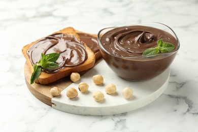 Photo of Tasty chocolate spread with mint and hazelnuts on white marble table, closeup
