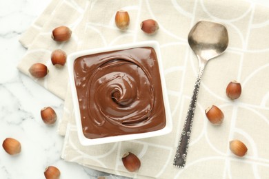 Photo of Tasty chocolate spread and hazelnuts on white table, flat lay