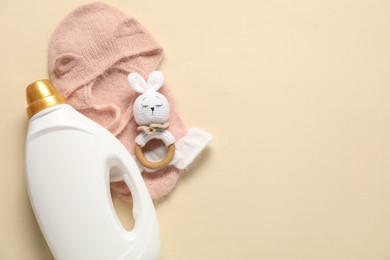 Photo of Bottle of fabric softener, toy and baby clothes on beige background, flat lay. Space for text