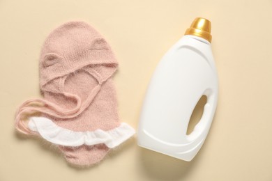 Photo of Bottle of fabric softener and baby clothes on beige background, flat lay