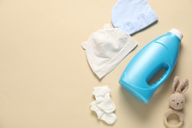 Photo of Bottle of fabric softener, toy and baby clothes on beige background, flat lay. Space for text