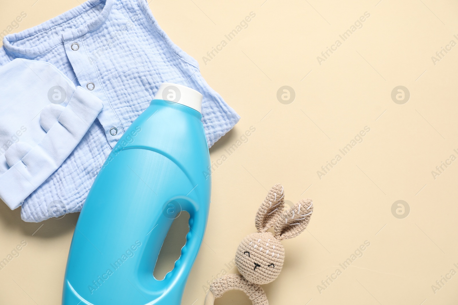 Bottle of fabric softener, toy and baby clothes on beige background, flat lay. Space for text Photo of Bottle of fabric softener, toy and baby clothes on beige background, flat lay. Space for text