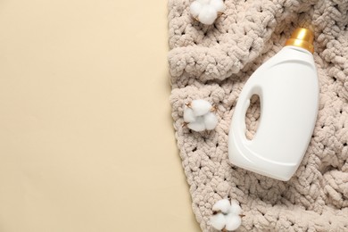 Photo of Bottle of fabric softener, cotton flowers and baby blanket on beige background, flat lay. Space for text