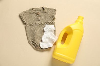 Photo of Bottle of fabric softener and baby clothes on beige background, flat lay