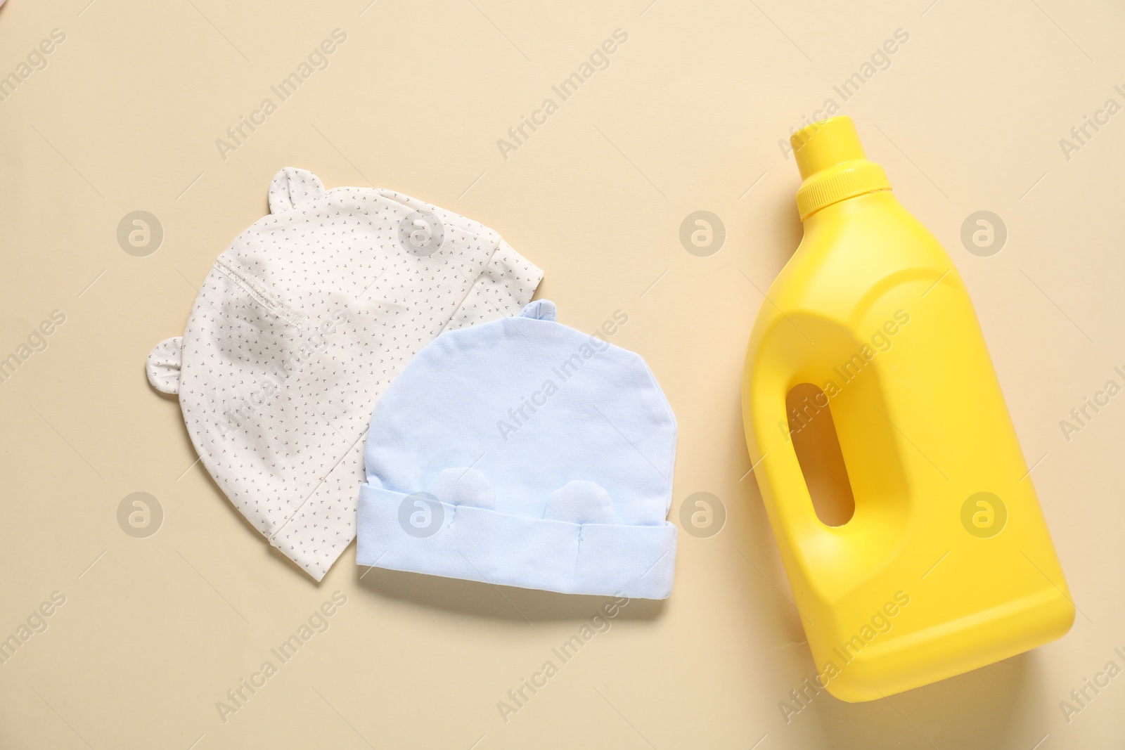 Bottle of fabric softener and baby hats on beige background, flat lay Photo of Bottle of fabric softener and baby hats on beige background, flat lay