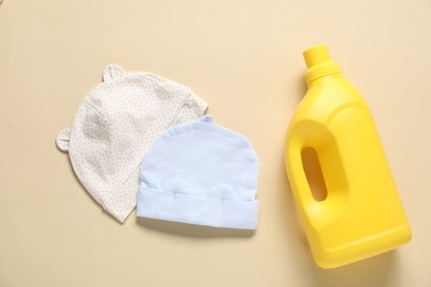 Photo of Bottle of fabric softener and baby hats on beige background, flat lay