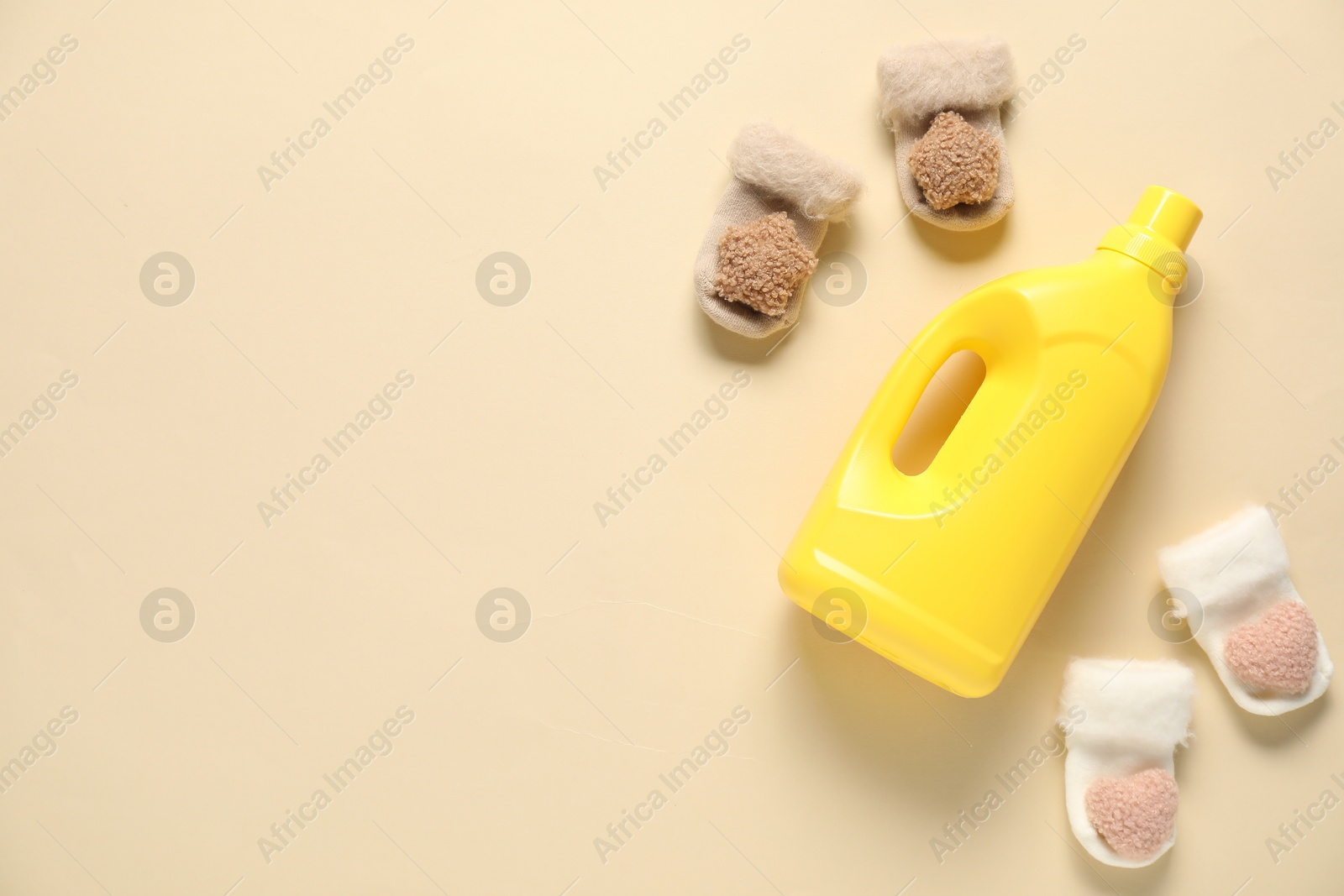 Bottle of fabric softener and baby socks on beige background, flat lay. Space for text Photo of Bottle of fabric softener and baby socks on beige background, flat lay. Space for text