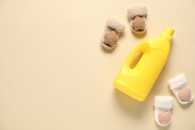 Photo of Bottle of fabric softener and baby socks on beige background, flat lay. Space for text