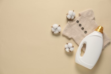 Photo of Bottle of fabric softener, cotton flowers and baby clothes on beige background, flat lay. Space for text