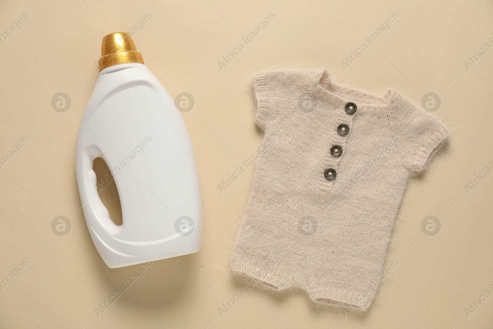 Bottle of fabric softener and baby clothes on beige background, flat lay Photo of Bottle of fabric softener and baby clothes on beige background, flat lay