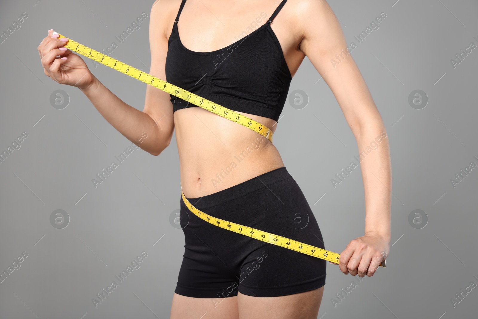 Woman with slim body and measuring tape on gray background, closeup Photo of Woman with slim body and measuring tape on gray background, closeup