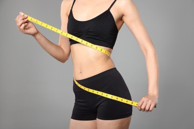 Photo of Woman with slim body and measuring tape on gray background, closeup