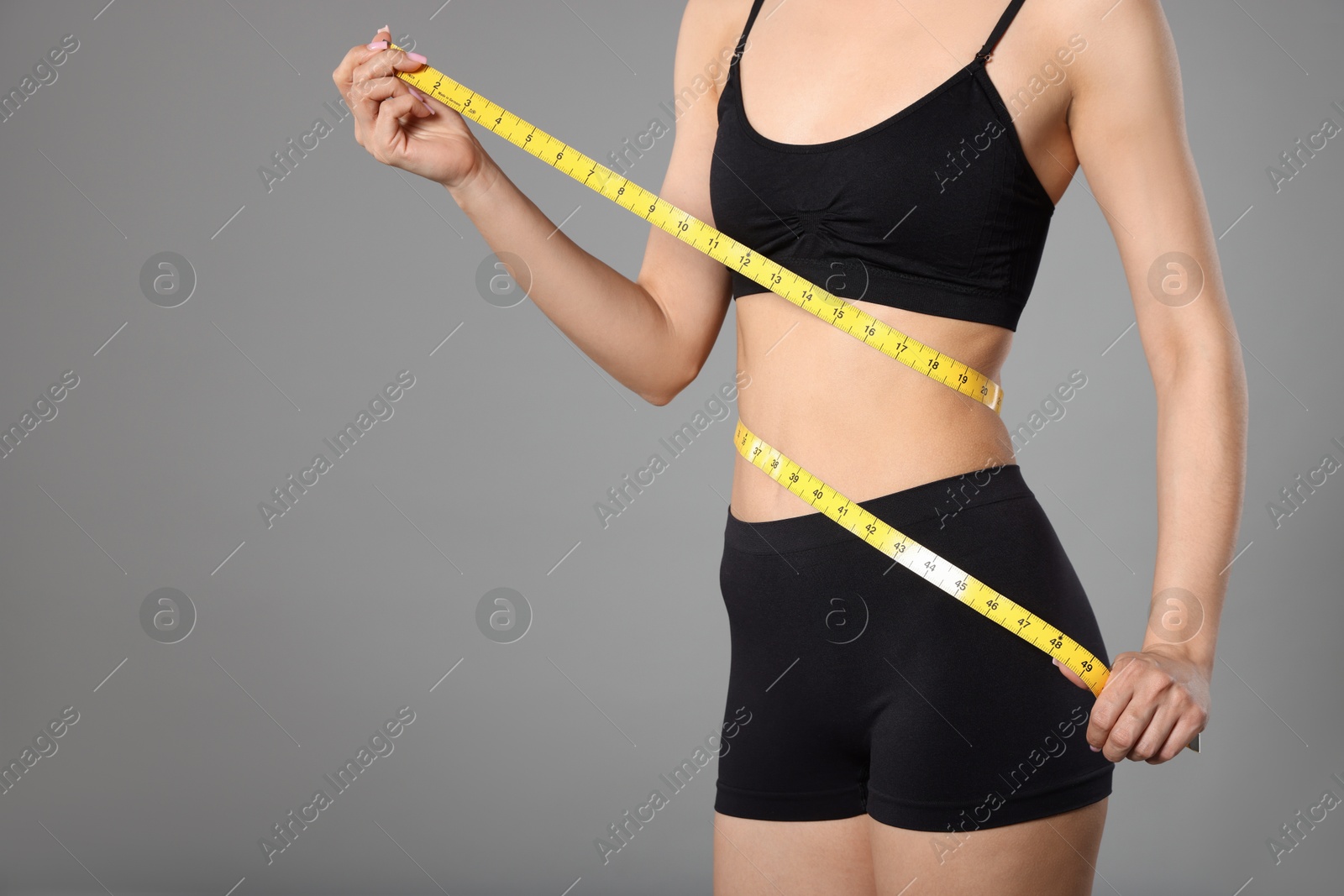 Woman with slim body and measuring tape on gray background, closeup. Space for text Photo of Woman with slim body and measuring tape on gray background, closeup. Space for text