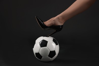 Photo of Woman in high heeled shoe with soccer ball on dark background, closeup