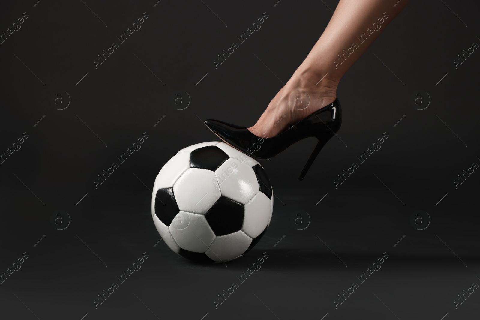 Woman in high heeled shoe with soccer ball on dark background, closeup Photo of Woman in high heeled shoe with soccer ball on dark background, closeup