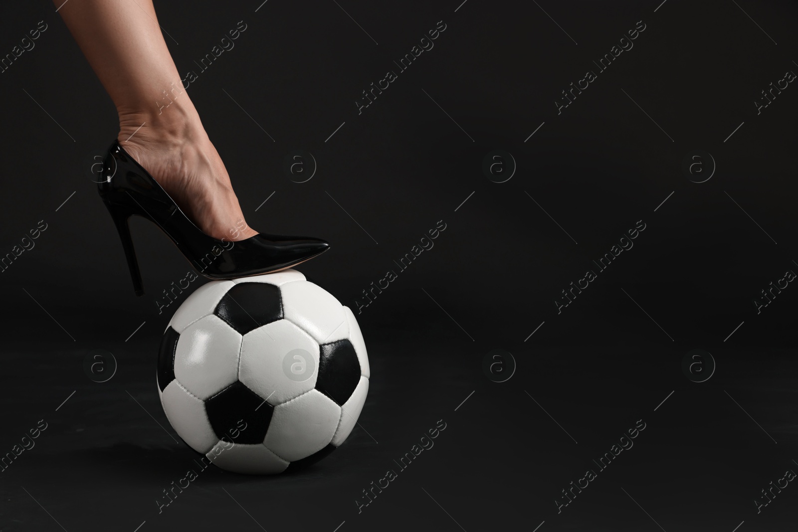 Woman in high heeled shoe with soccer ball on dark background, closeup. Space for text Photo of Woman in high heeled shoe with soccer ball on dark background, closeup. Space for text