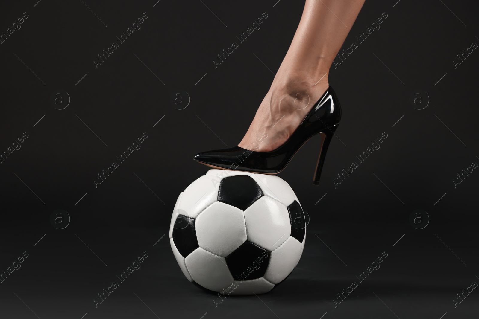 Photo of Woman in high heeled shoe with soccer ball on dark background, closeup