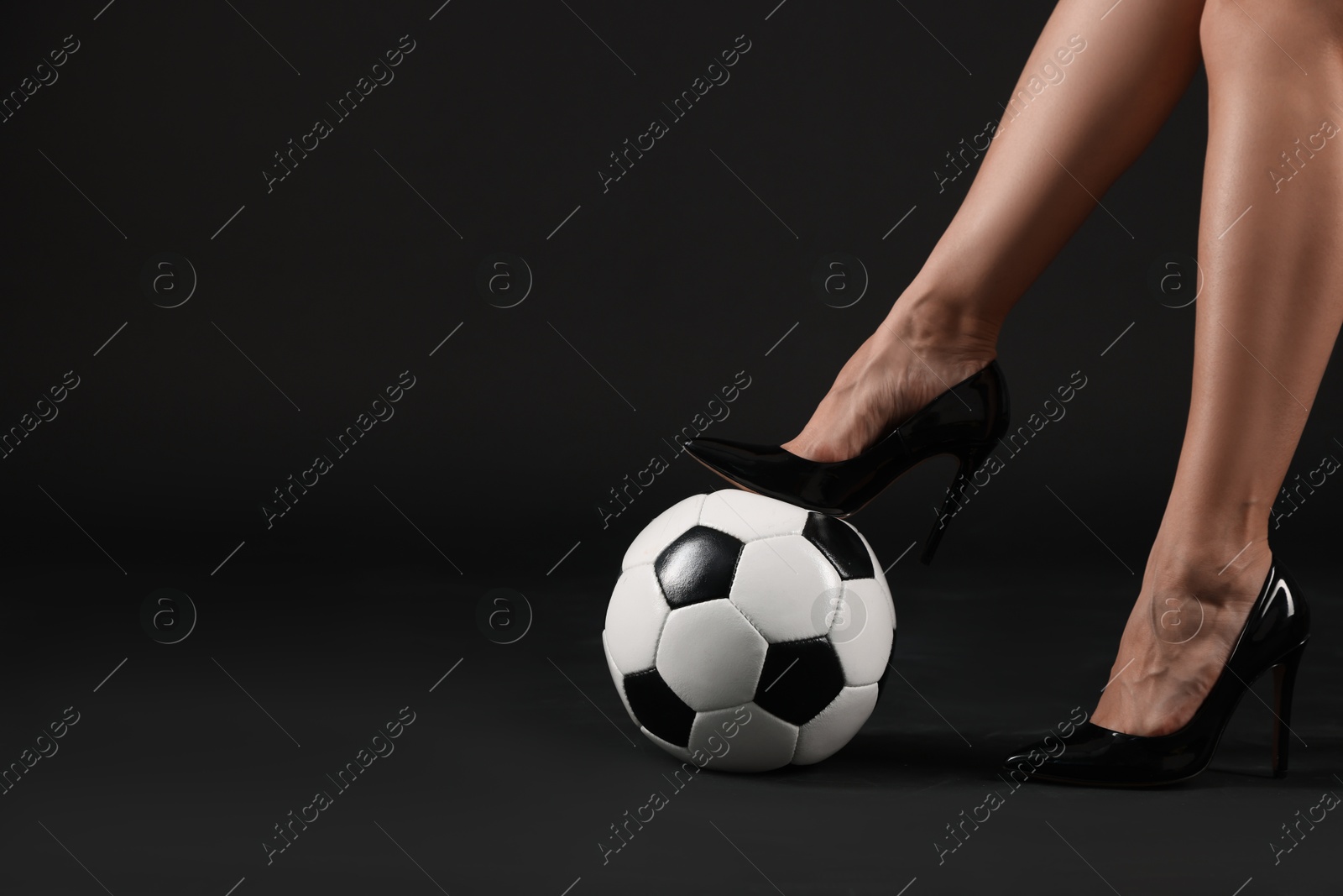 Photo of Woman in high heeled shoes with soccer ball on dark background, closeup. Space for text