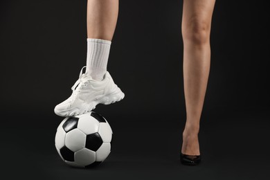 Photo of Woman in high heeled shoe and sneaker with soccer ball on dark background, closeup